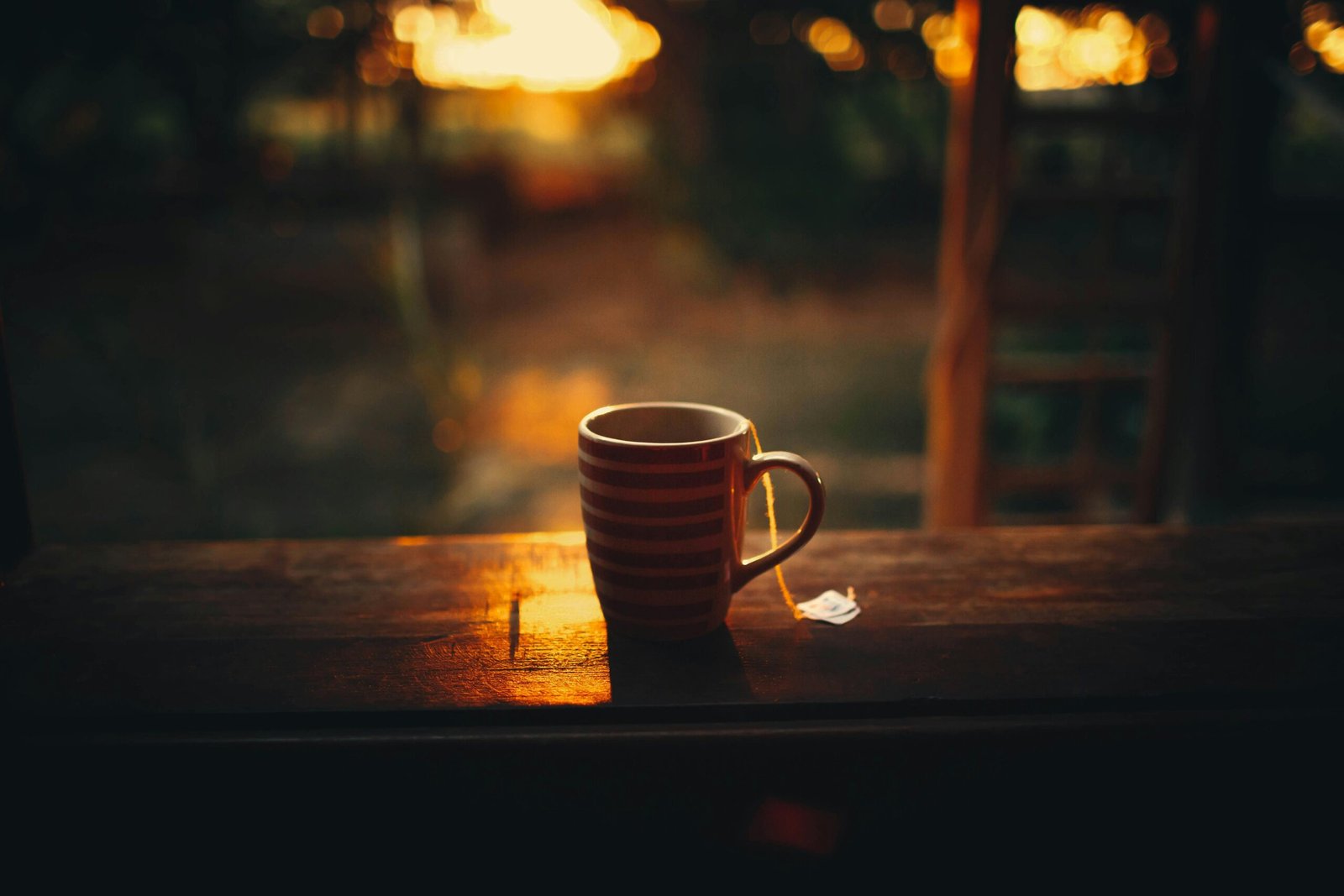 From above of cup of hot tea placed on balcony wooden railing against blurred green forest during bright sunrise