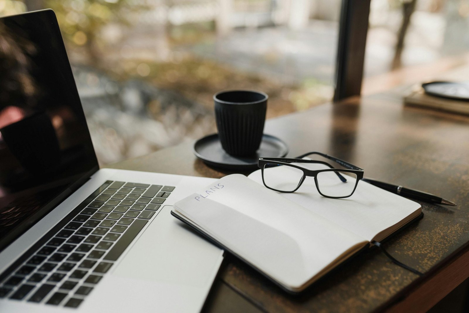 A cozy workspace featuring an open laptop, notepad, glasses, and coffee on a wooden desk.